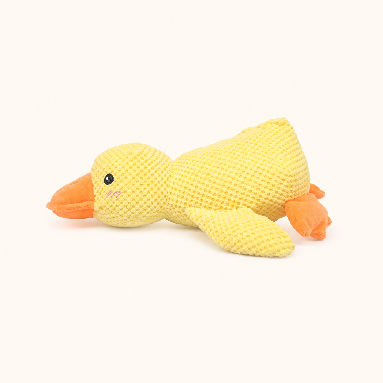 Small yellow plush squeaky duck dog toy on cream background