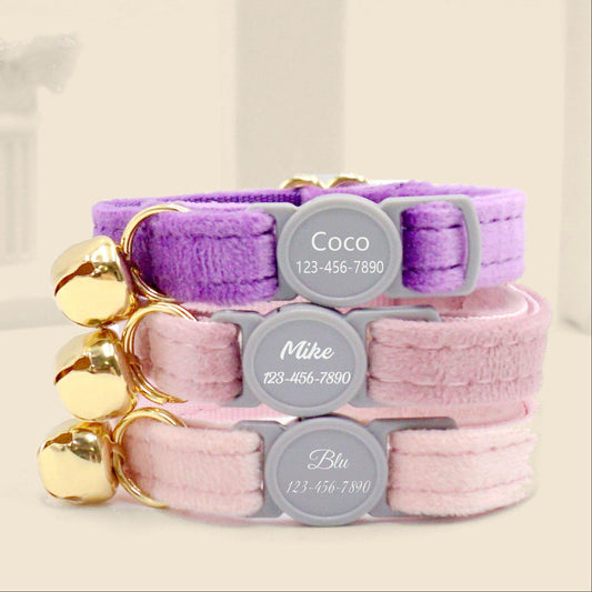 Personalised velvet cat collars with engraved name tags stacked on a beige background